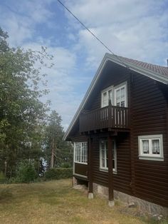 a brown house sitting on top of a lush green field next to a tall forest