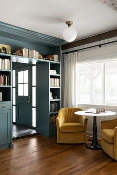 two chairs and a table in a room with bookshelves on either side of the window