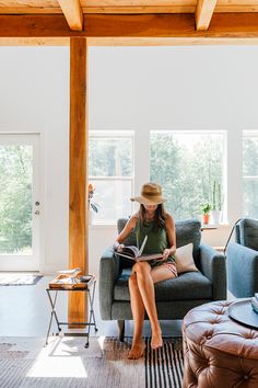 a woman sitting on a couch in a living room reading a book while wearing a cowboy hat