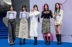 four women standing in front of a wall with their hands together and looking at their cell phones