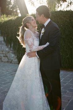 a bride and groom standing together in front of a hedge at sunset with their arms around each other