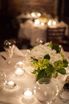 a vase filled with white and green flowers on top of a table covered in candles