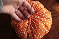 a person is holding an orange and white polka dot fabric ball on a wooden table