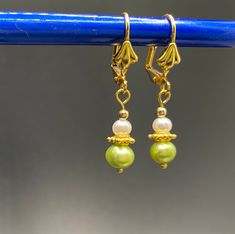 Tiny dainty green and white pearl earrings with a touch of vermeil gold dangle from gold plated leverback shell earwire. Perfect for a spring wedding or any garden party. The earrings are about 5/8 inch long, measured from the end of the earwire. Comes nestled comfortably on a bed of cotton in a white jewelry box. NA-822-0624-1111 Green Pearl Drop Earrings, Green Dangle Pearl Earrings, Green Pearl Dangle Earrings, Green Pearl Charm Drop Earrings, Formal Green Pearl Drop Earrings, Green Dangle Pearl Earrings With Ear Wire, White Jewelry Box, White Pearl Earring, Spring Wedding