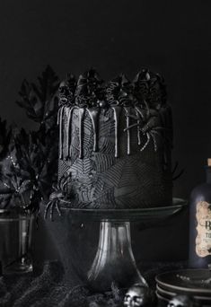 a black cake sitting on top of a table next to two bottles and plates filled with food