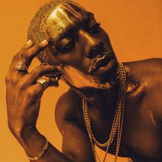 a man with gold paint on his face and necklaces around his neck, holding a cell phone to his ear