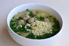 a white bowl filled with soup and meatballs on top of green leafy greens