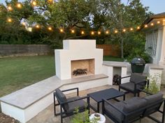 an outdoor fireplace and seating area with string lights strung above the fire place, surrounded by lawn furniture