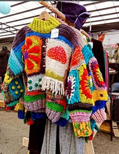 a colorful crocheted jacket is hanging on a rack at an outdoor flea market