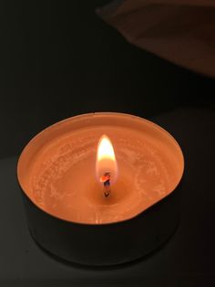 a lit candle sitting on top of a black table next to a white bowl filled with liquid