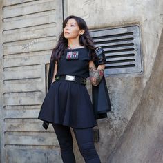 a woman standing next to a wall with her hand on her hip and wearing black gloves