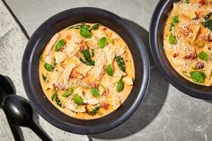 two black bowls filled with pasta and spinach on top of a gray table next to utensils