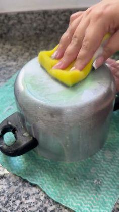 a person using a yellow sponge to clean a metal container on top of a green towel