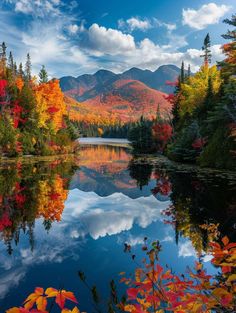 a lake surrounded by trees with fall foliage on the shore and mountains in the background