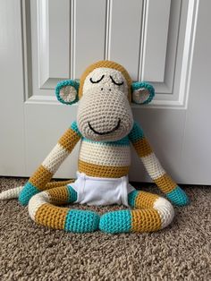 a crocheted monkey sitting on the floor in front of a door with its eyes closed