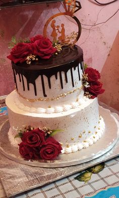 a three tiered cake with chocolate frosting and red roses on top, sitting on a table