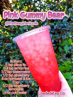 the pink gummy bear drink is being held up in front of some bushes and trees