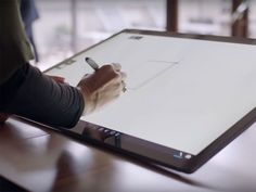 a person is writing on a whiteboard with a pen in their hand while sitting at a table