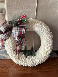 a knitted wreath with a candy cane and pine cone on top sitting on a wooden table