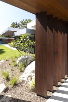 an outside view of a house with rocks and plants in the foreground, and grass on the other side