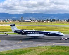 an airplane that is sitting on the tarmac with grass and mountains in the background