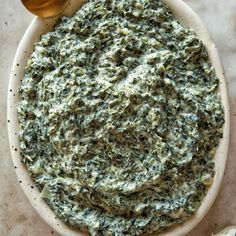 spinach dip in a bowl with a spoon next to it on a marble surface