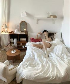 a woman is laying in bed with her legs up on the headboard and reading