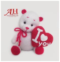 a crocheted white teddy bear holding a red heart with the word i love you written on it