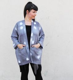 a woman standing in front of a white wall wearing a gray and white polka dot cardigan