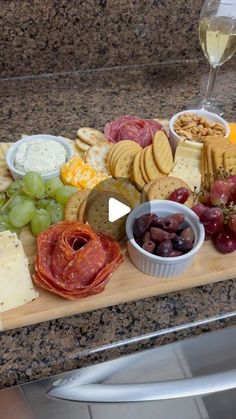 a wooden cutting board topped with cheese, crackers and grapes next to a glass of wine