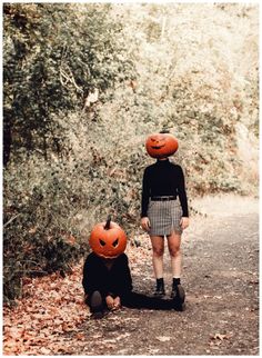 two people with pumpkins on their heads walking down a path in the woods together