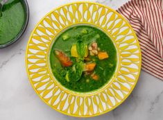 a yellow and white bowl filled with green soup next to a red and white striped napkin