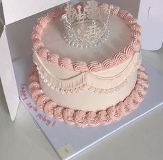 a three layer cake with pink frosting and a tiara on top