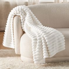 a white couch covered in a blanket on top of a shaggy rug next to a window