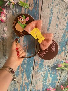 a hand is holding up a minnie mouse ears headband with a cartoon character on it