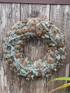 a wreath is hanging on the side of a wooden fence with moss and pine cones