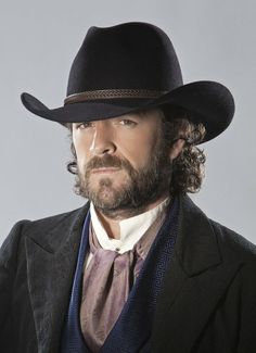 a man with a beard wearing a black cowboy hat and suit jacket, looking off to the side