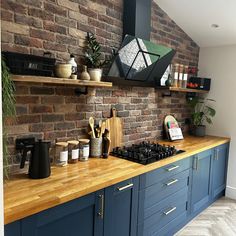 a kitchen with blue cabinets and wooden counter tops next to a brick wall that has shelves on it