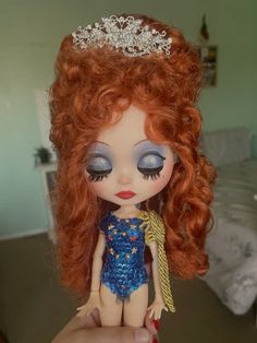 a close up of a doll with red hair and blue eyes wearing a tiara