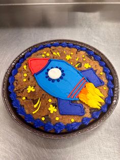 a cake shaped like a rocket ship on top of a metal surface with yellow and blue icing