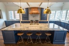 a large kitchen with blue cabinets and marble counter tops, two pendant lights over the island