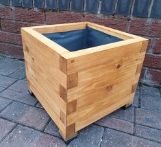 a wooden planter sitting on top of a brick floor next to a wall and sidewalk