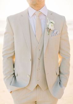 a man in a suit and tie standing on the beach with his hands in his pockets