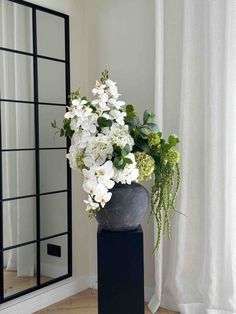 a vase with white flowers and greenery on a table in front of a mirror