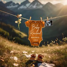 a baby's bodysuit hanging on a clothesline with mountains in the background