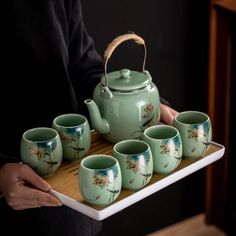 a person holding a tray with tea cups and a teapot on top of it