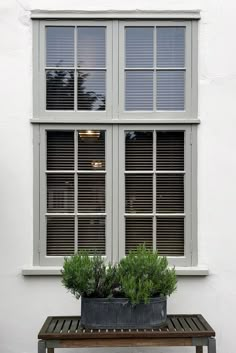 a bench sitting in front of a window with two potted plants next to it