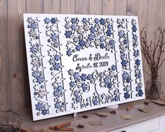 a white and blue wedding guest sign sitting on top of a wooden table next to dried flowers