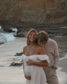 two people are hugging on the beach by the water's edge, with waves crashing in to shore behind them