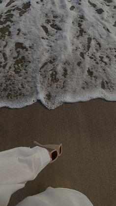 someone's feet in the sand at the beach with waves coming in from the water